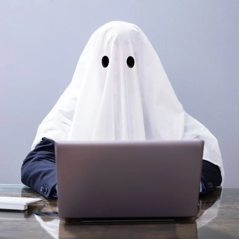 Ghostwriting services: a ghost writer under a white sheet working on a laptop — the invisible writer behind your content